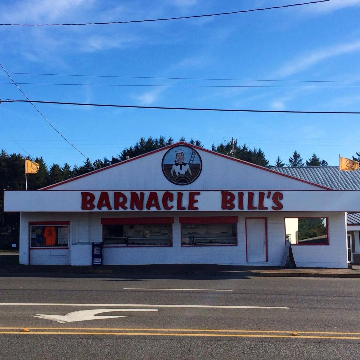 Front view of Barnacle Bill's seafood restaurant: white building with red trim and a large red sign across the facade, blue sky above.